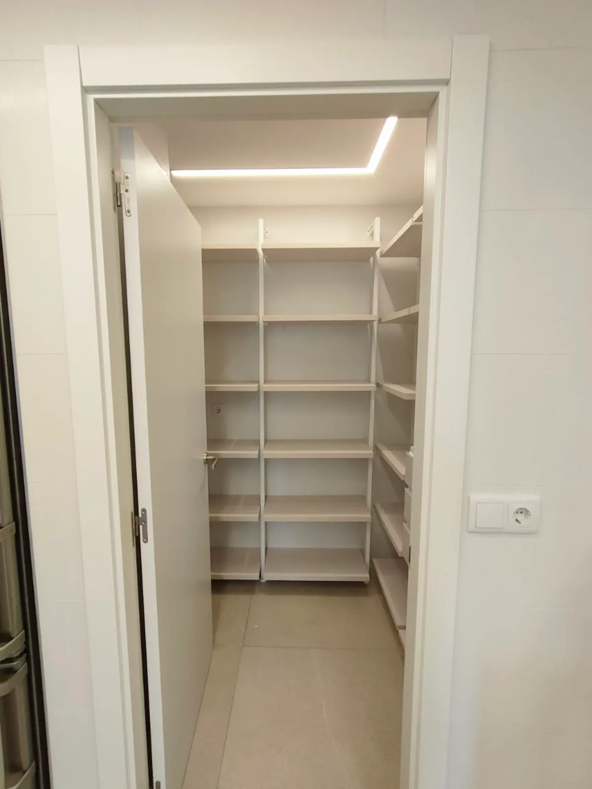 Despensa cerrada con estanterías integrada en reforma de cocina residencial.