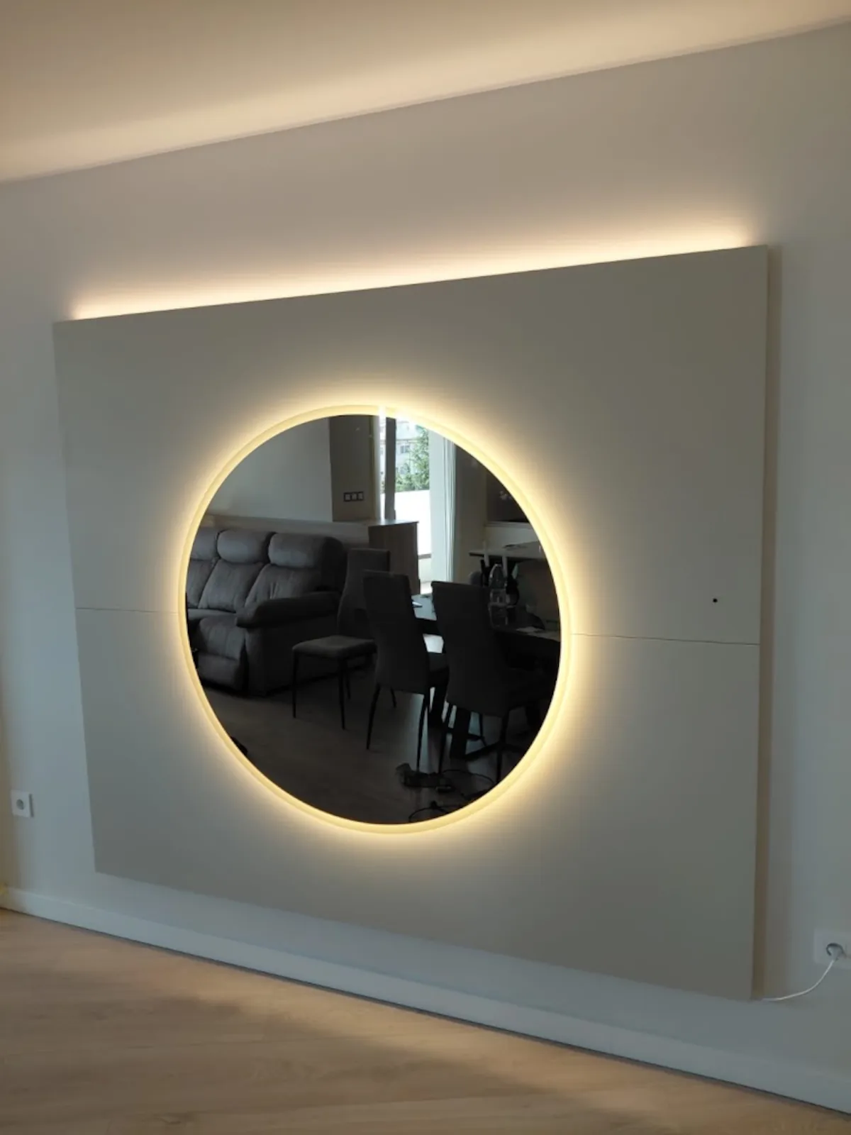 Panel a medida con espejo circular e iluminación indirecta en la zona de comedor