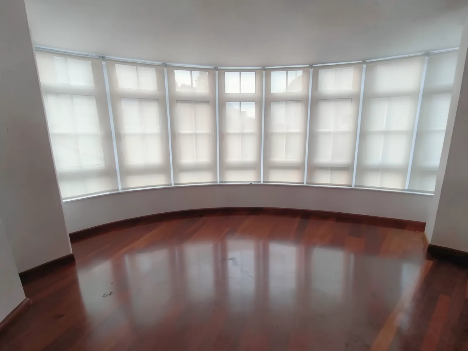 Zona de estar vacía con frente curvo de ventanas antes de definir el sofá a medida.